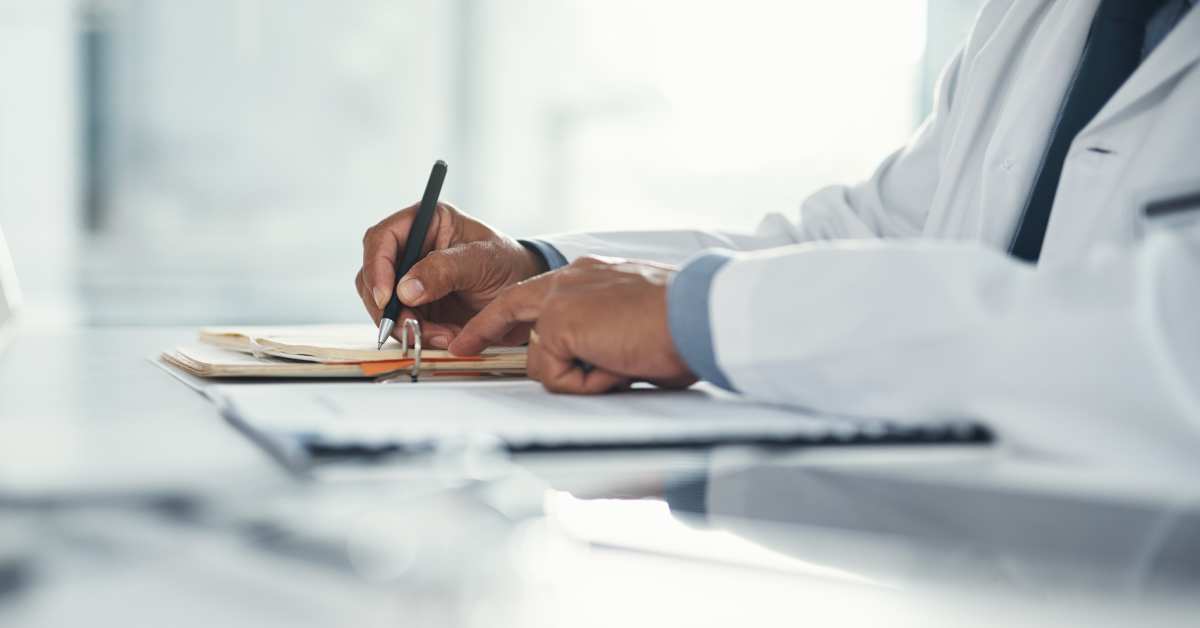 doctor hands writing on paper or document at a desk in the hospital healthcare professional drafting a medical insurance letter legal paperwork or form a gp filing a document in a clinic office