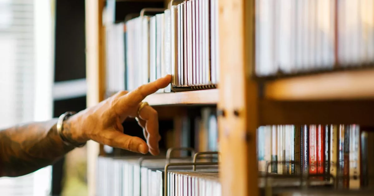 0 man searching through cds on a bookshelf with his hand