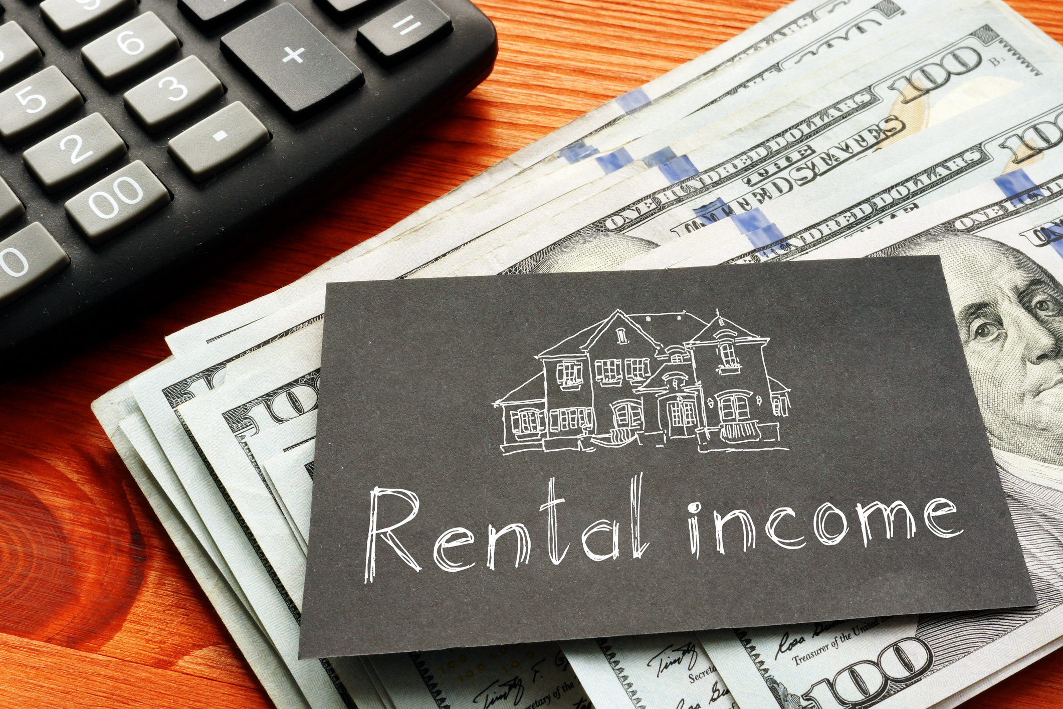 a card with rental income sitting on top of cash next to a calculator