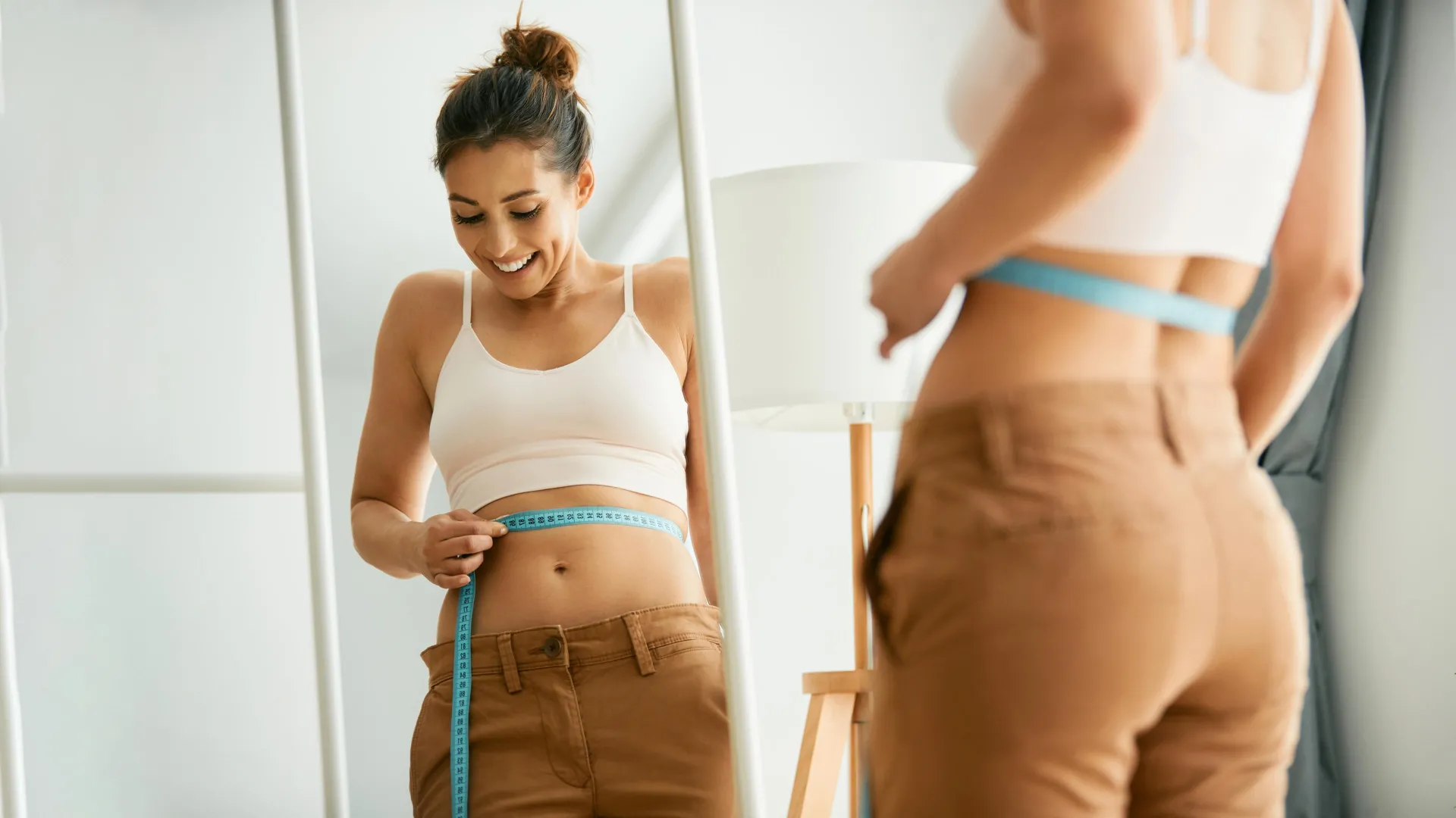 happy woman measuring waist in mirror