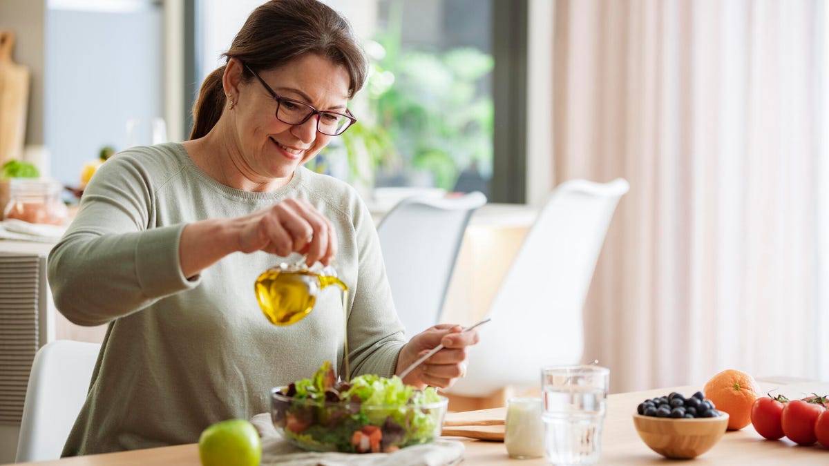 woman pouring olive oil on salad