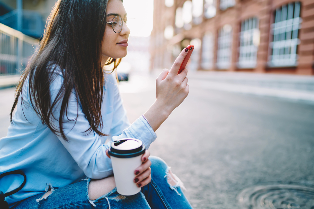 A young woman with glasses and lon hair using real apps that pay cash on her mobile device