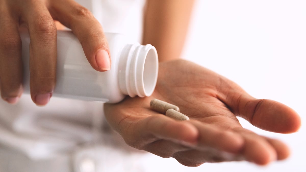 Hand with pink fingernails tipping two supplement capsules into palm